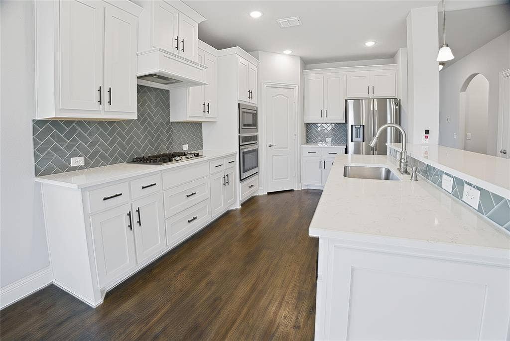 620 Shadow Trail, Frisco, TX 75033 Contemporary kitchen featuring white cabinetry with dark hardware, a herringbone tile backsplash, integrated stainless steel appliances, light-toned countertops, and wood-finish flooring