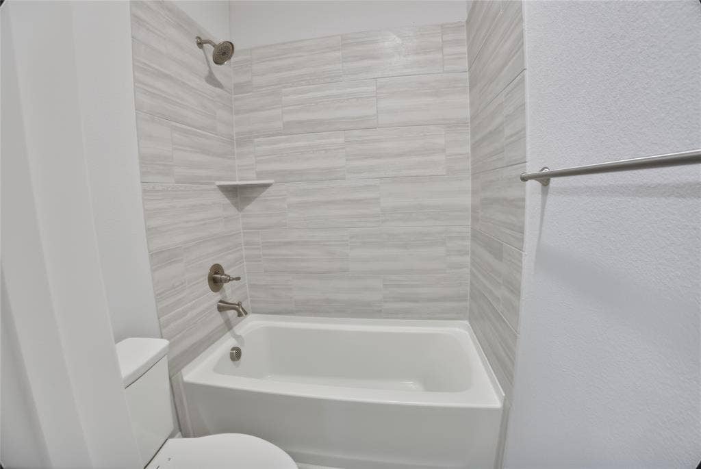 620 Shadow Trail, Frisco, TX 75033 Bathtub and shower combination featuring brushed nickel fixtures, a built-in corner shelf, and light gray horizontal tile surround