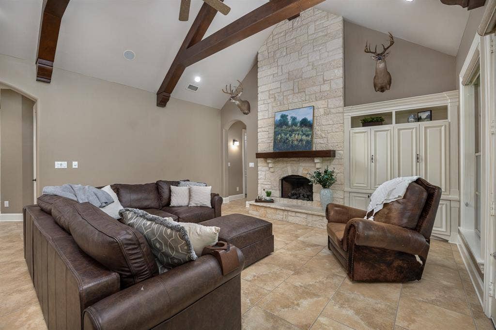 1915 Stonegate Valley Drive, Tyler, TX 75703 Vaulted ceiling with exposed wood beams, stone fireplace, built-in cabinetry, arched doorways, and tile flooring