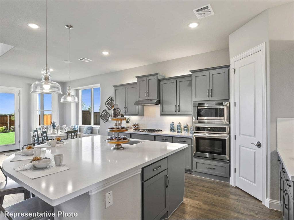 1317 Staffords Point Lane, Anna, TX 75409 Kitchen featuring an expansive island with a light-toned countertop, gray cabinetry, stainless steel appliances including a built-in oven and microwave, and wood-finish flooring