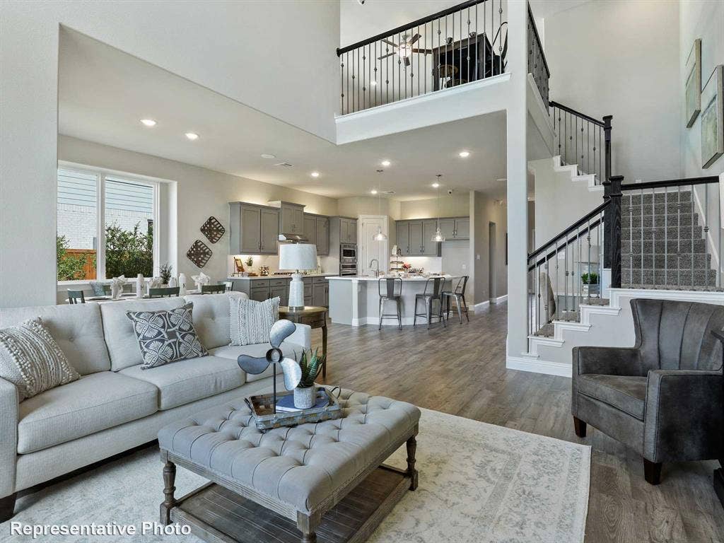 1317 Staffords Point Lane, Anna, TX 75409 Open-concept living area with wood-finish flooring, a two-story ceiling, and a prominent staircase with black wrought iron spindles