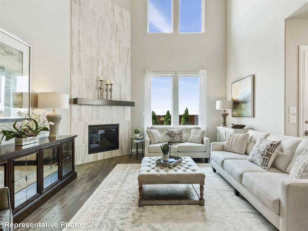 1317 Staffords Point Lane, Anna, TX 75409 Great room featuring a two-story ceiling, a floor-to-ceiling tiled fireplace surround with a dark wood mantel, wood-finish flooring, and multiple large windows