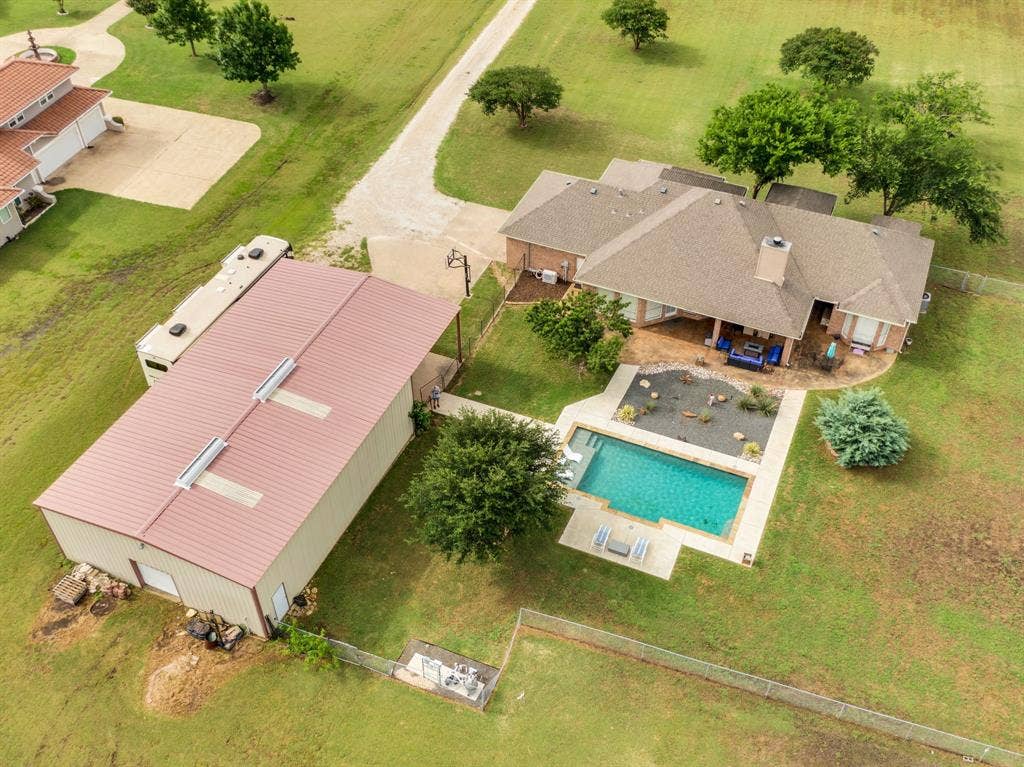431 Mcalpin Road, Midlothian, TX 76065 Expansive property featuring a rectangular swimming pool with concrete decking, a covered patio, a detached metal-sided outbuilding with a metal roof, and a gravel driveway