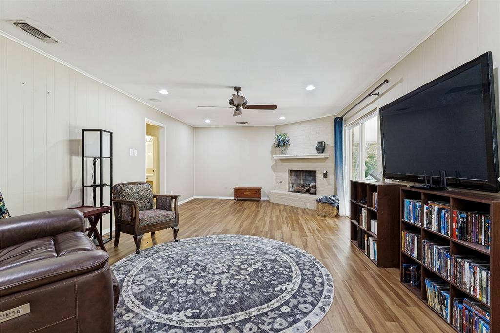 1121 W Redbud Drive, Hurst, TX 76053 Spacious living area featuring wood-finish flooring, a corner fireplace with a white brick surround and mantel, recessed lighting, and a ceiling fan