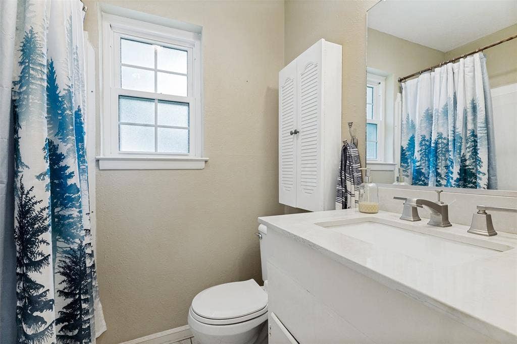 1121 W Redbud Drive, Hurst, TX 76053 Bathroom featuring a white vanity with an integrated sink, brushed nickel faucet, wall-mounted mirror, and a window with privacy glass