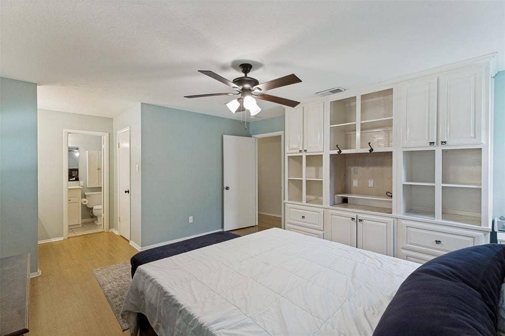 1121 W Redbud Drive, Hurst, TX 76053 Bedroom featuring extensive built-in cabinetry with glass-front uppers and lower drawers, wood-finish flooring, and a ceiling fan
