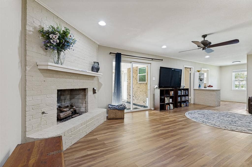 1121 W Redbud Drive, Hurst, TX 76053 Spacious living area featuring a brick fireplace with hearth, wood-finish flooring, recessed lighting, and a ceiling fan