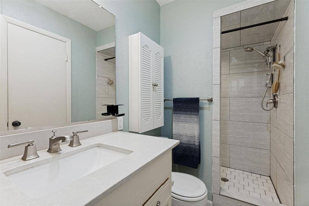 1121 W Redbud Drive, Hurst, TX 76053 Bathroom featuring a white vanity with an integrated sink, brushed nickel faucet, large mirror, and a walk-in shower with light-toned rectangular wall tiles and hexagonal floor tiles