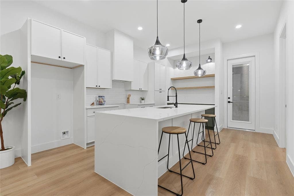 2212 Marburg Street, Dallas, TX 75215 Contemporary kitchen featuring a large waterfall-edge island with seating, white shaker cabinetry, and wood-finish flooring