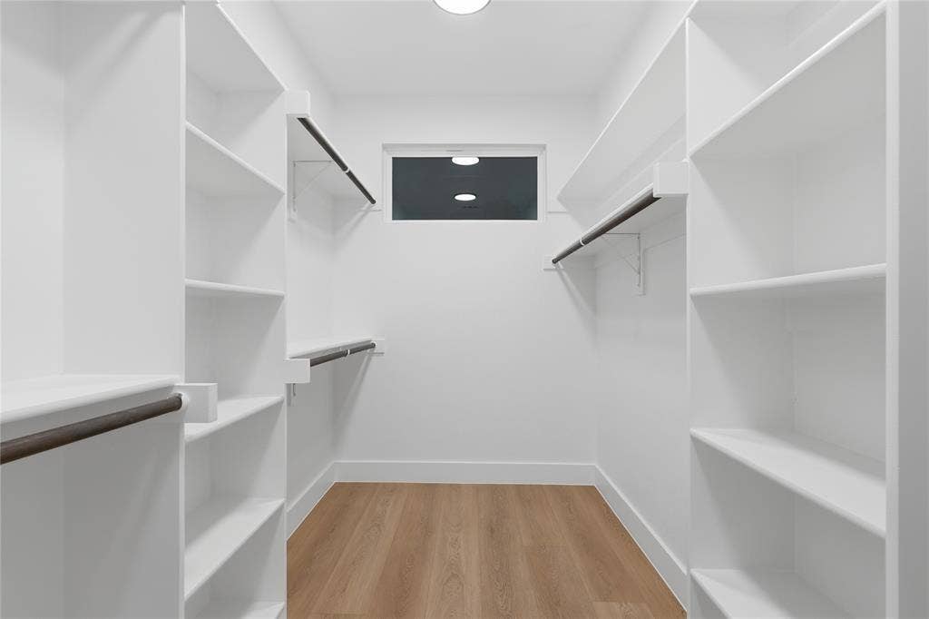 2212 Marburg Street, Dallas, TX 75215 Walk-in closet featuring extensive white shelving, multiple hanging rods, a transom window, wood-finish flooring, and bright overhead lighting