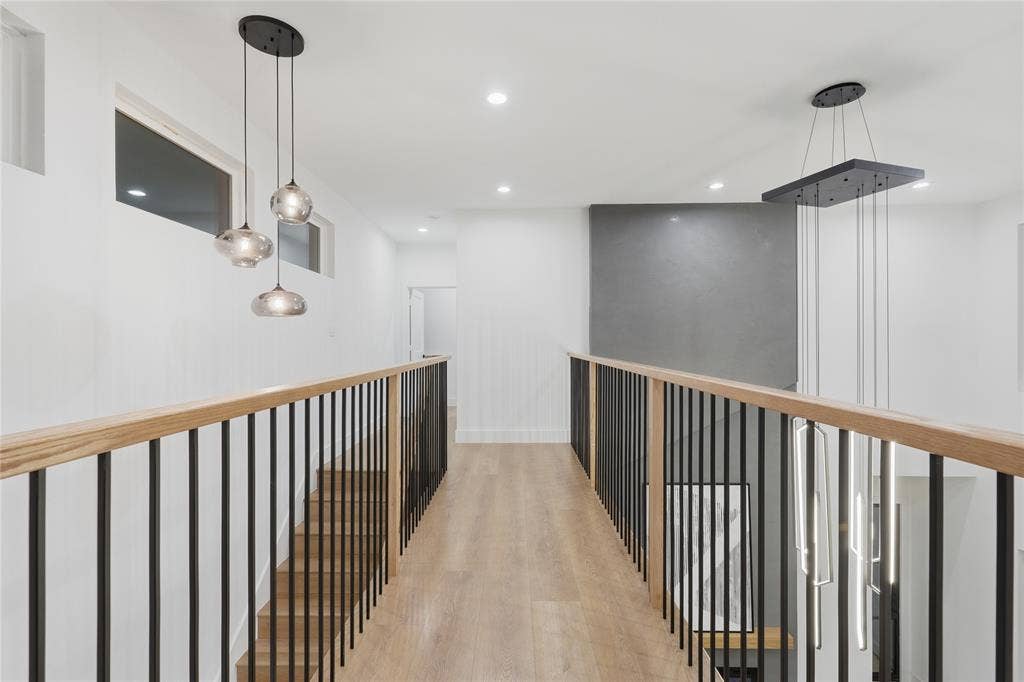 2212 Marburg Street, Dallas, TX 75215 Upper-level hallway featuring wood-finish flooring, contemporary lighting fixtures, a light wood handrail with black iron balusters, recessed ceiling lights, and transom windows