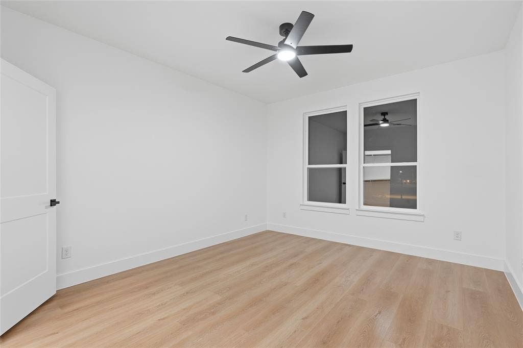 2212 Marburg Street, Dallas, TX 75215 Bright room featuring two large windows, a ceiling fan with integrated lighting, wood-finish flooring, and a contemporary white door with matte black hardware