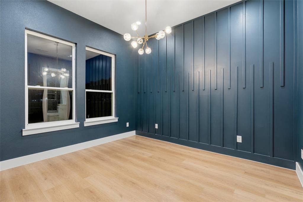 2212 Marburg Street, Dallas, TX 75215 Room featuring a decorative accent wall with vertical paneling, two double-hung windows, wood-finish flooring, and a modern chandelier with spherical lights