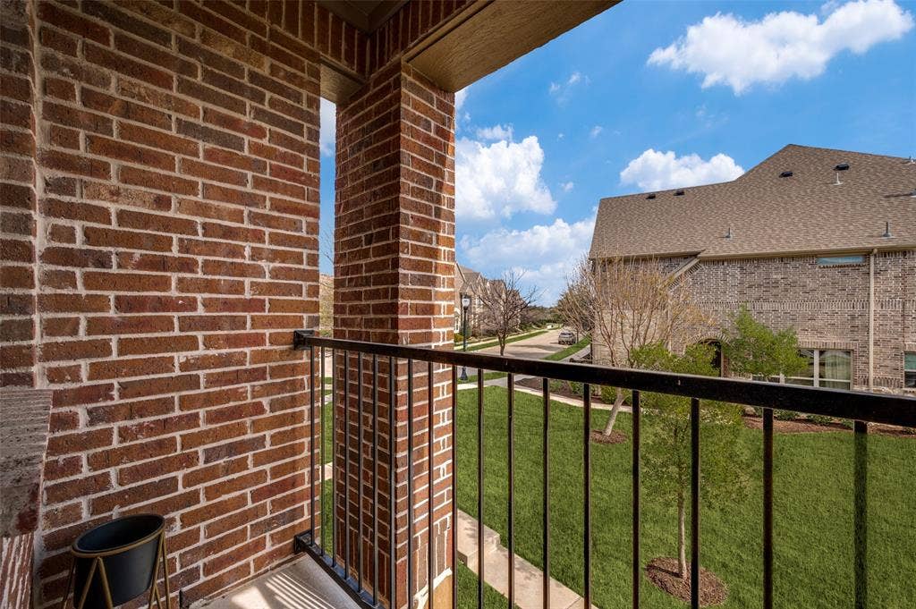 7424 Mitchell Drive, McKinney, TX 75070 Covered balcony at 7424 Mitchell Drive McKinney Texas with brick surround and iron railing, providing private outdoor living space and neighborhood views, ideal for buyers searching for a McKinney TX townhome with balcony, outdoor seating area, and relaxing spot in a quiet Collin County subdivision.