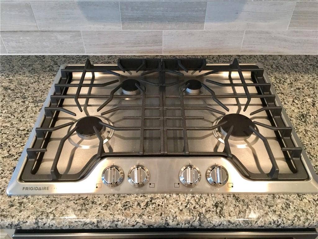 7424 Mitchell Drive, McKinney, TX 75070 Close up of kitchen showing stainless steel gas cooktop, oven, detailed tile backsplash, stone counters, and modern controls, appealing to buyers searching for a McKinney Texas townhouse with stainless steel appliances, gas cooking, and stylish kitchen design in a convenient Collin County location near major roads and retail.