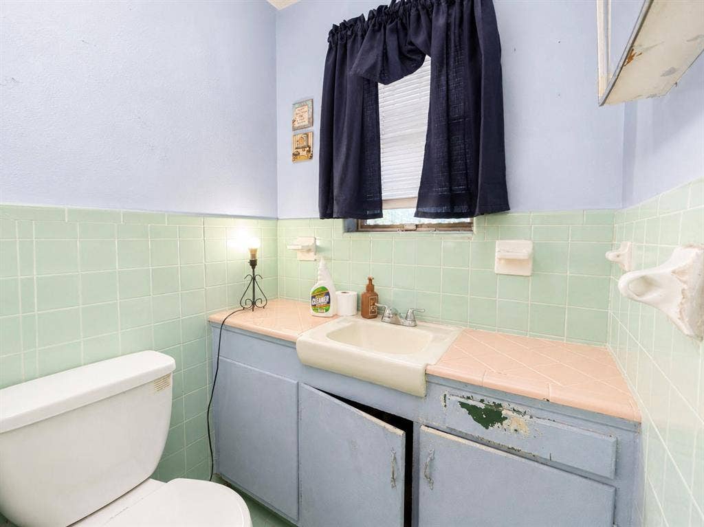 3023 Carpenter Avenue, Dallas, TX 75215 Bathroom featuring light blue wall paint, green square wall tiles, a built-in vanity with a pink countertop and integrated sink, and a white toilet