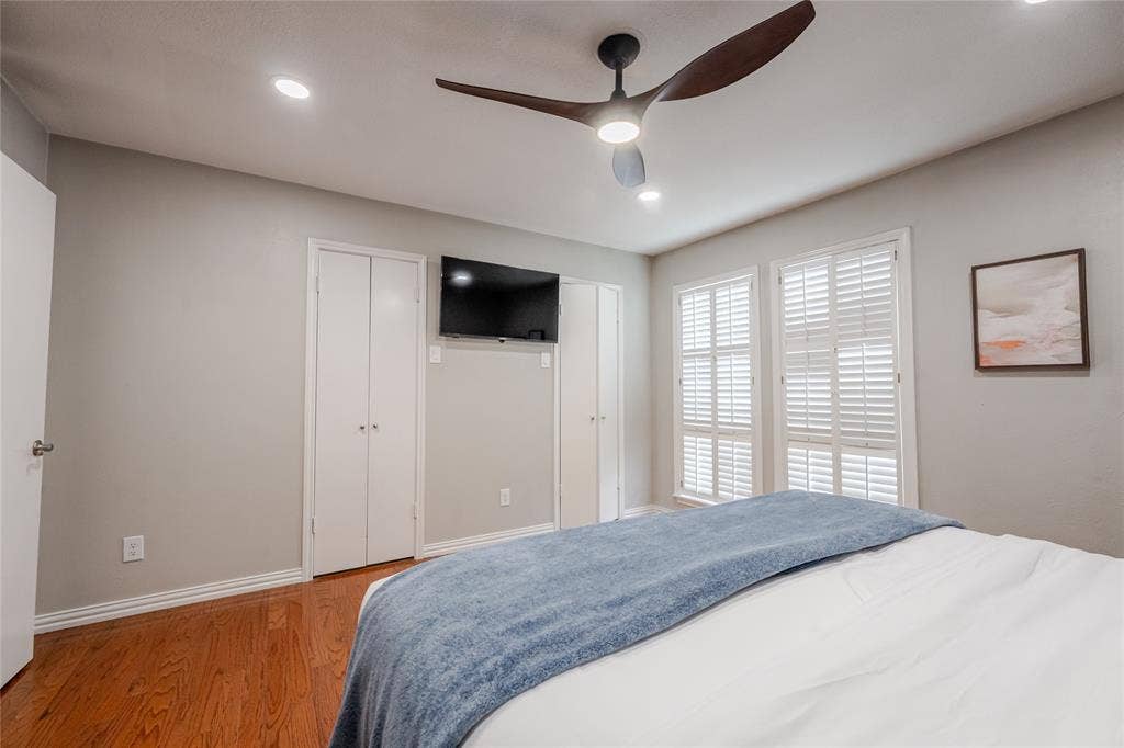 15221 Berry Trail, #1201, Dallas, TX 75248 Bedroom featuring wood-finish flooring, two sets of white plantation shutters, and a modern ceiling fan with integrated lighting