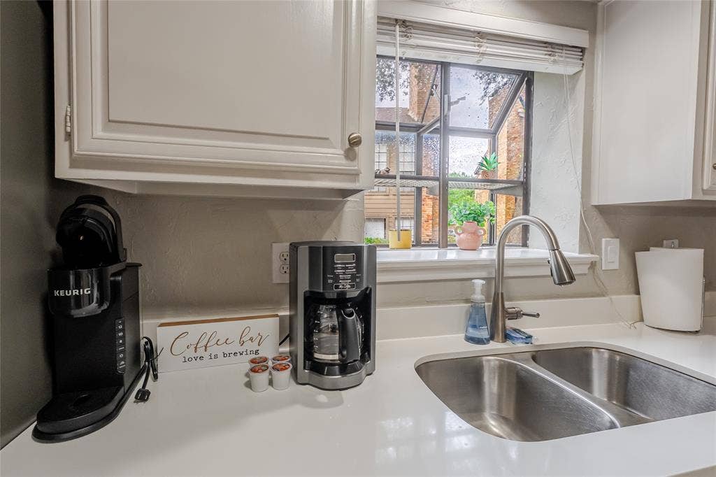 15221 Berry Trail, #1201, Dallas, TX 75248 Kitchen window featuring a dual basin stainless steel sink, gooseneck faucet, light-toned countertops, and upper cabinetry with silver-tone hardware