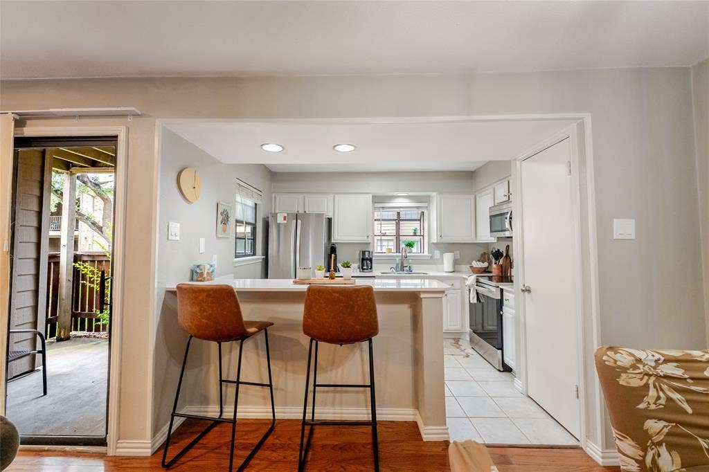15221 Berry Trail, #1201, Dallas, TX 75248 Kitchen featuring white cabinetry, stainless steel appliances, recessed lighting, and a breakfast bar with a light-colored countertop