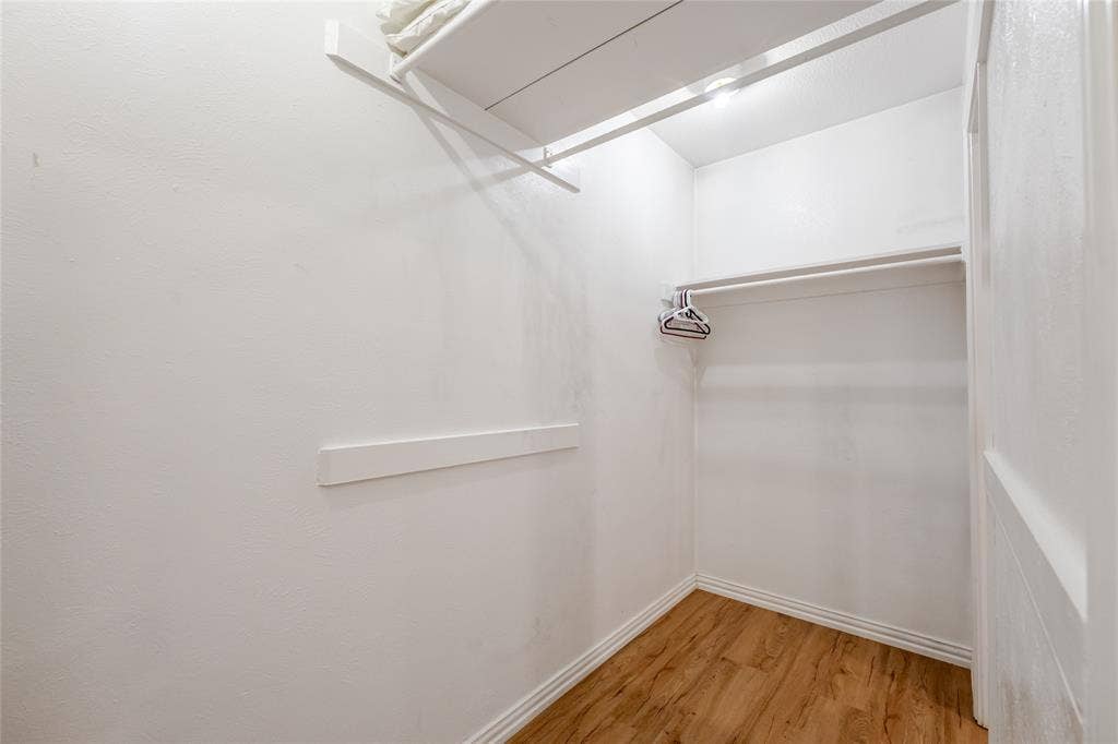 15221 Berry Trail, #1201, Dallas, TX 75248 Walk-in closet featuring wood-finish flooring, white baseboards, and built-in shelving with a hanging rod