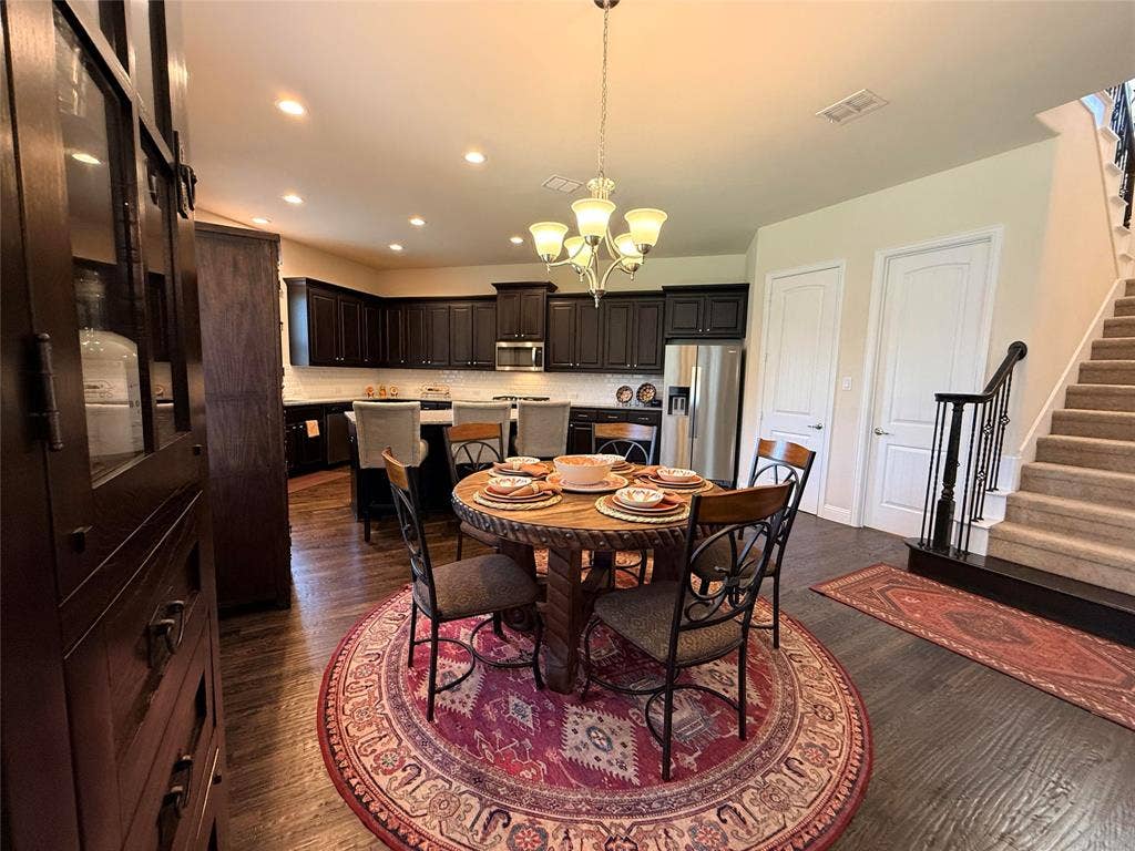 7310 Venice Drive, #4, Grand Prairie, TX 75054 Kitchen and dining area featuring wood-finish flooring, dark wood cabinetry, a central island with white countertops, stainless steel appliances, and a staircase with an ornamental iron railing