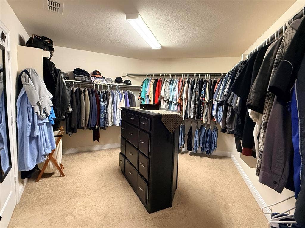 7310 Venice Drive, #4, Grand Prairie, TX 75054 Expansive walk-in closet featuring extensive built-in shelving, multiple hanging rods, a central storage island with drawers, plush carpet flooring, and a full-length mirrored door