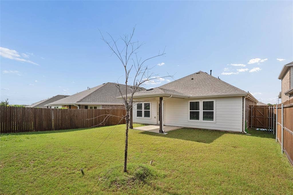 317 Fire Rock Drive, Royse City, TX 75189 Expansive backyard featuring a green lawn, wood privacy fencing, and a covered patio with a concrete slab