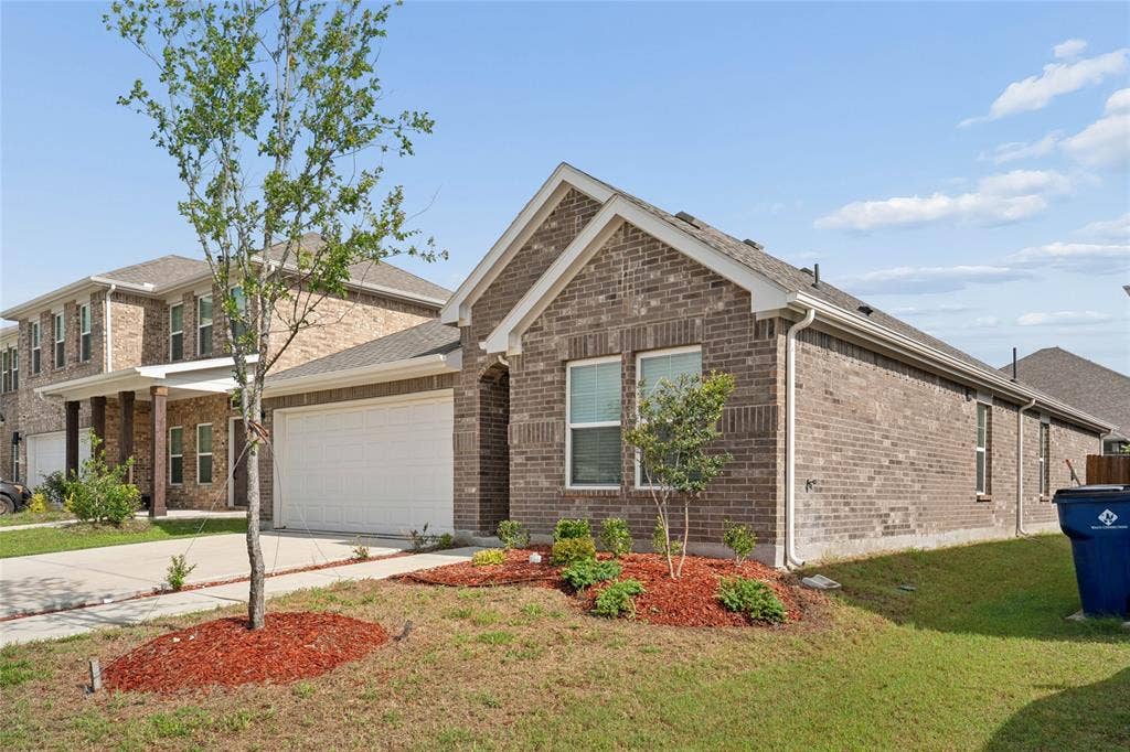 317 Fire Rock Drive, Royse City, TX 75189 Brick facade residence featuring a two-car garage, pitched shingle roof, and white-framed windows