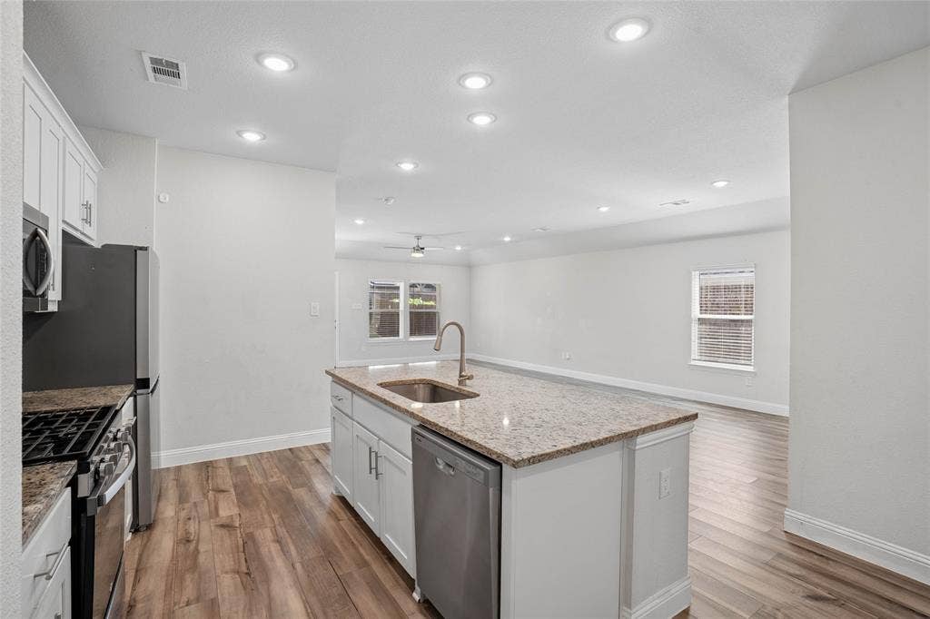 317 Fire Rock Drive, Royse City, TX 75189 Open-concept kitchen featuring an expansive center island with an undermount sink, granite-style countertops, white cabinetry, and wood-finish flooring