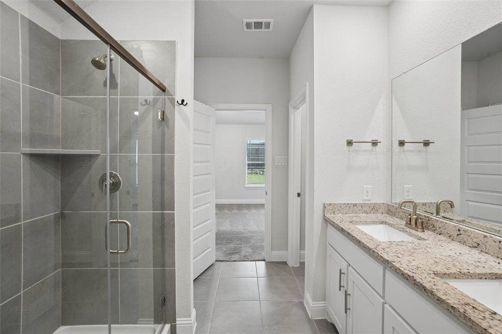 317 Fire Rock Drive, Royse City, TX 75189 Bathroom featuring a glass-enclosed shower with tile surround, a dual vanity with light-toned countertops, and light-colored flooring