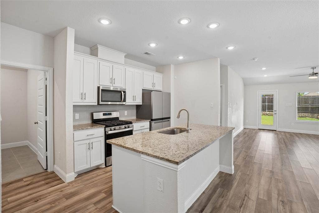 317 Fire Rock Drive, Royse City, TX 75189 Modern kitchen featuring an island with an undermount sink, granite countertops, white cabinetry, stainless steel appliances, and wood-finish flooring