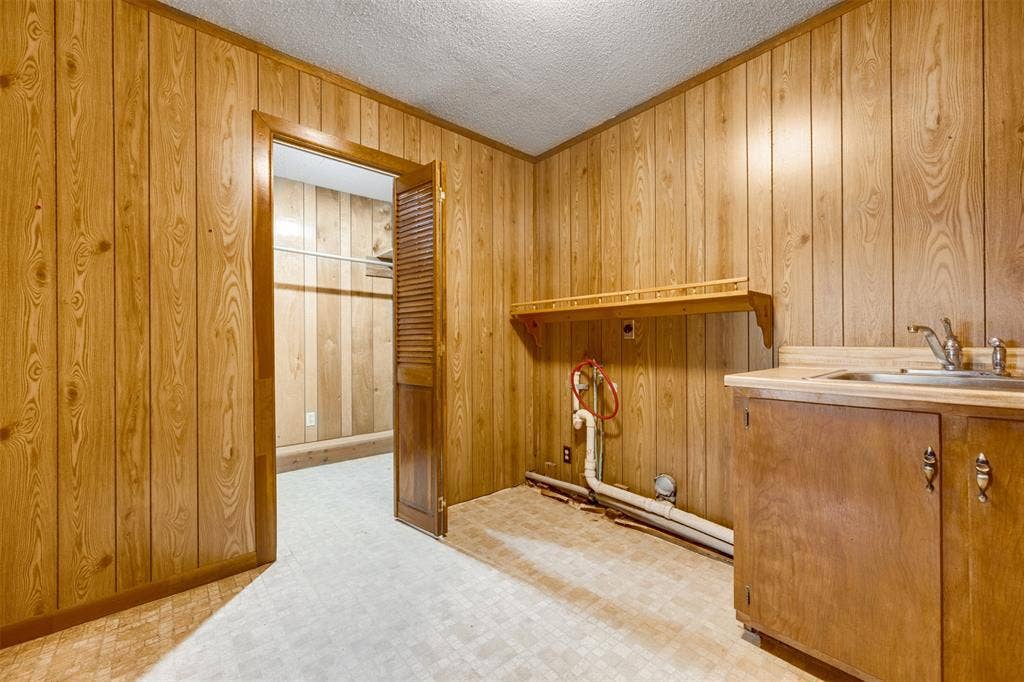 8798 Hill N Dale Road, Tyler, TX 75709 Utility room featuring wood-finish paneling, a built-in countertop with an integrated sink, base cabinetry, and a wall-mounted shelf