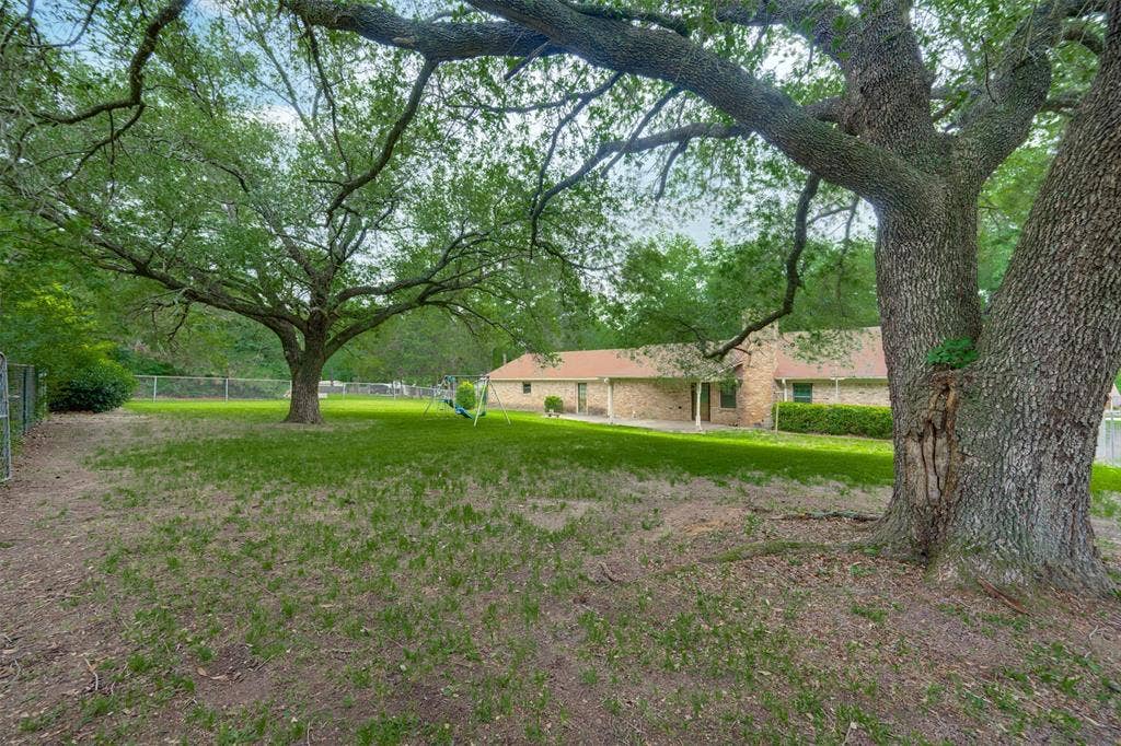 8798 Hill N Dale Road, Tyler, TX 75709 Expansive backyard featuring mature trees, a manicured lawn, and a perimeter chain-link fence