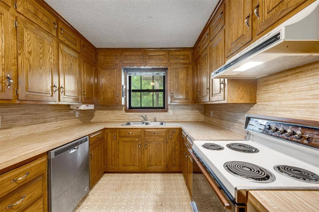 8798 Hill N Dale Road, Tyler, TX 75709 U-shaped kitchen featuring wood cabinetry, laminate countertops, a stainless steel dishwasher, a white electric range with overhead ventilation, and a double basin sink beneath a window
