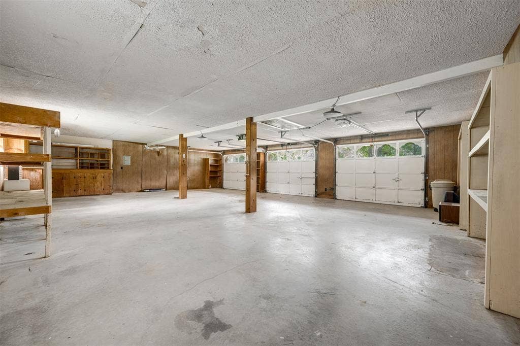 8798 Hill N Dale Road, Tyler, TX 75709 Spacious garage featuring a concrete floor, two white overhead garage doors with window inserts, exposed structural beams, and built-in shelving and cabinetry for storage