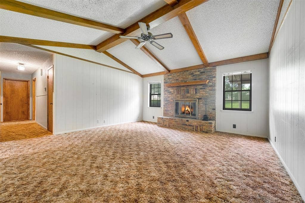 8798 Hill N Dale Road, Tyler, TX 75709 Spacious living area featuring a vaulted ceiling with exposed wood beams, a brick-surround fireplace with a wood mantle, and paneled walls