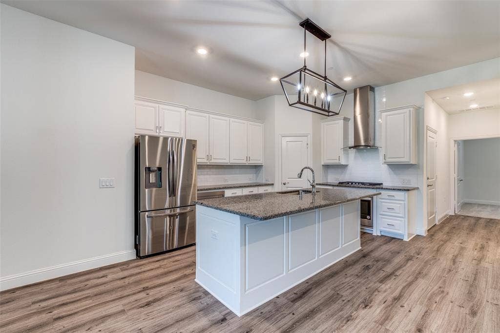 3930 Dalea Drive, Prosper, TX 75078 Spacious kitchen featuring an oversized island with a sink, stainless steel appliances, white cabinetry, granite countertops, and wood-finish flooring
