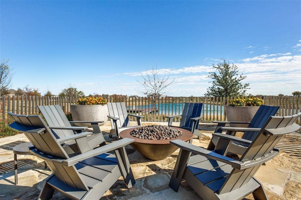 3930 Dalea Drive, Prosper, TX 75078 Stone patio with a built-in fire pit, surrounded by a wood fence, concrete planters, and a body of water
