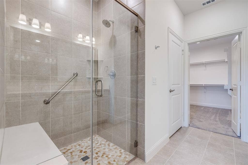 3930 Dalea Drive, Prosper, TX 75078 Tiled walk-in shower with a glass enclosure, integrated bench, and decorative pebble flooring