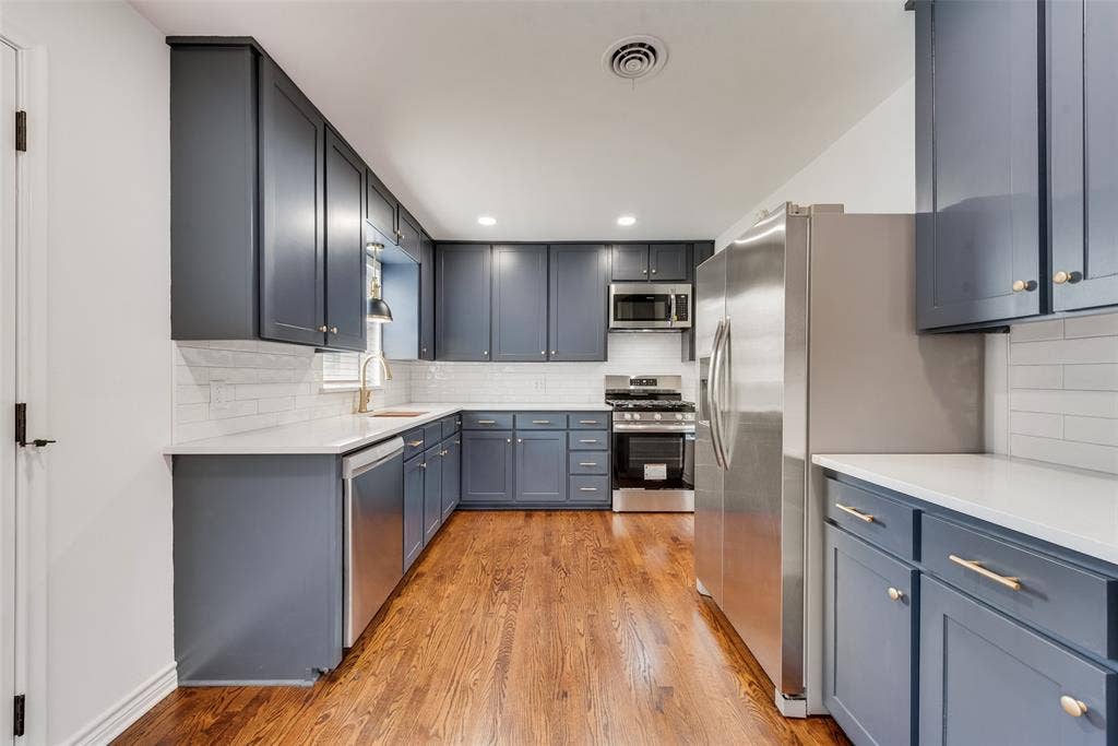 2523 San Medina Avenue, Dallas, TX 75228 Kitchen featuring wood-finish flooring, white subway tile backsplash, light countertops, and dark cabinetry with brass hardware