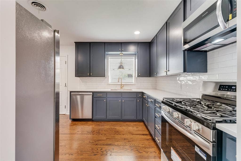2523 San Medina Avenue, Dallas, TX 75228 Contemporary kitchen featuring dark cabinetry, stainless steel appliances, a subway tile backsplash, light countertops, and wood-finish flooring