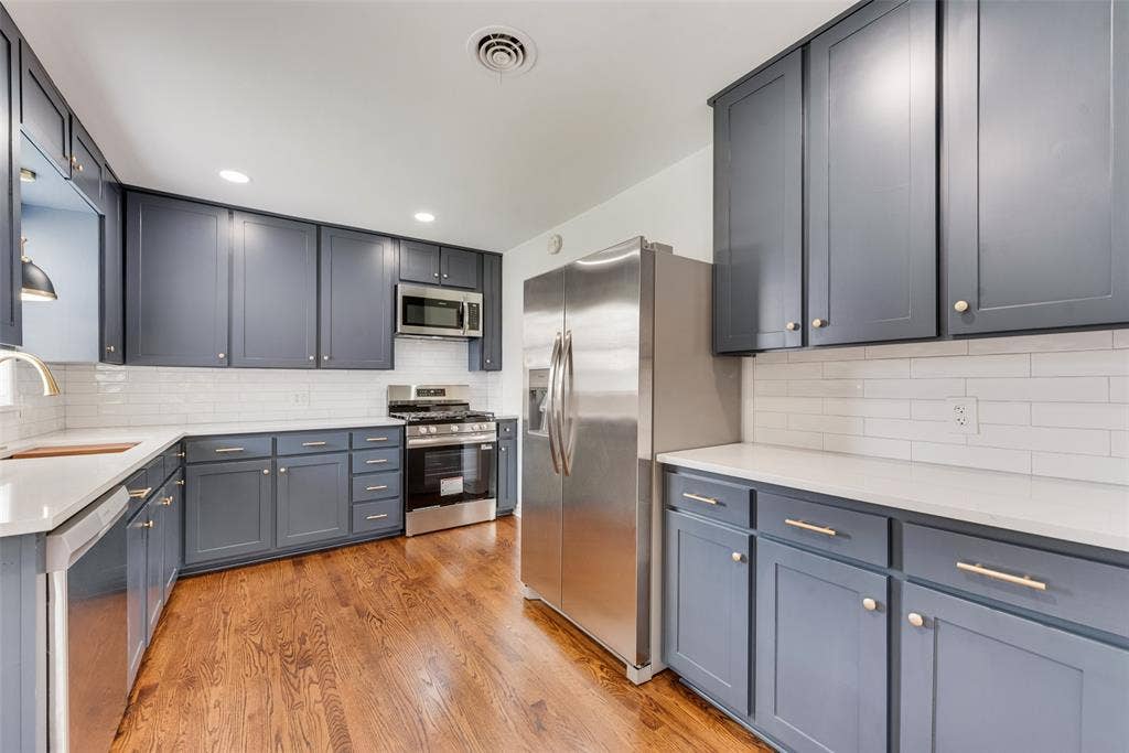 2523 San Medina Avenue, Dallas, TX 75228 Kitchen featuring dark gray cabinetry, stainless steel appliances, a white subway tile backsplash, light-colored countertops, and wood-finish flooring