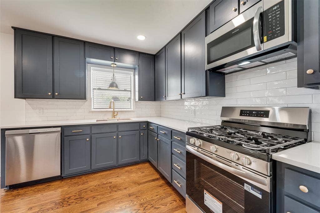 2523 San Medina Avenue, Dallas, TX 75228 Kitchen featuring dark cabinetry, stainless steel appliances, a white subway tile backsplash, light countertops, and wood-finish flooring