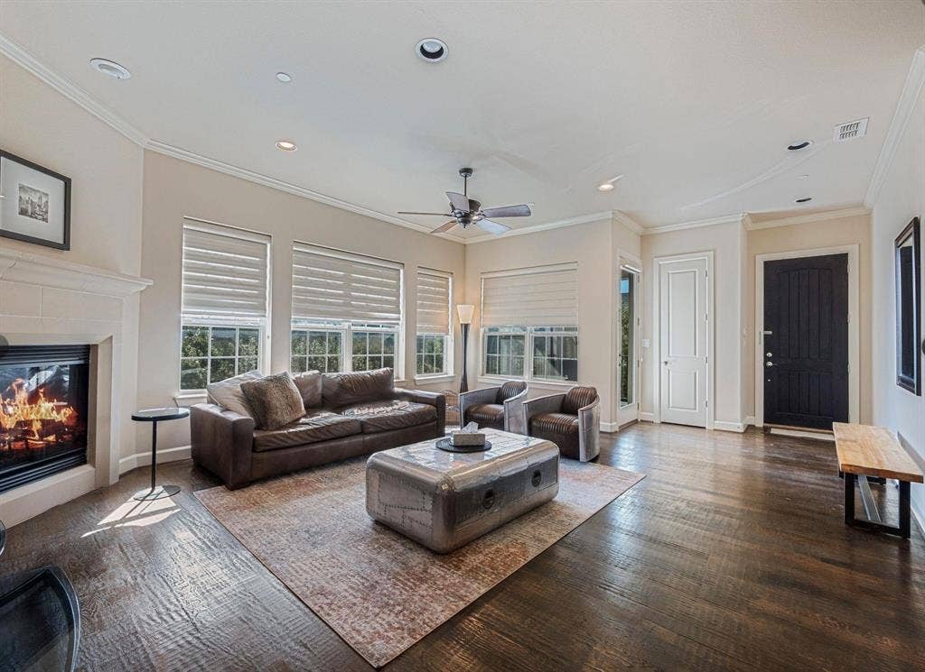 5001 Meridian Lane, #2103, Addison, TX 75001 Spacious living area featuring dark wood flooring, a fireplace with a stone surround, multiple windows with blinds, crown molding, and recessed lighting