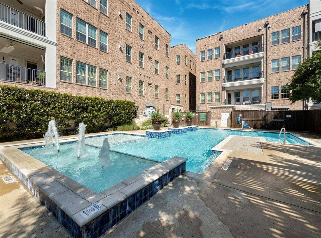 5001 Meridian Lane, #2103, Addison, TX 75001 Outdoor swimming pool with integrated fountains, blue mosaic tile accents, surrounding concrete decking, and lush perimeter landscaping