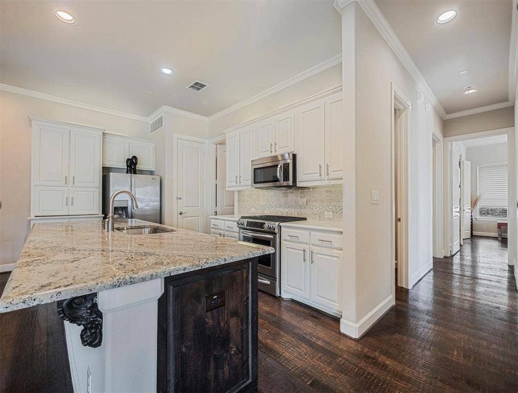 5001 Meridian Lane, #2103, Addison, TX 75001 Gourmet kitchen featuring a granite island with an undermount sink, stainless steel appliances, white cabinetry, decorative tile backsplash, and dark wood-finish flooring