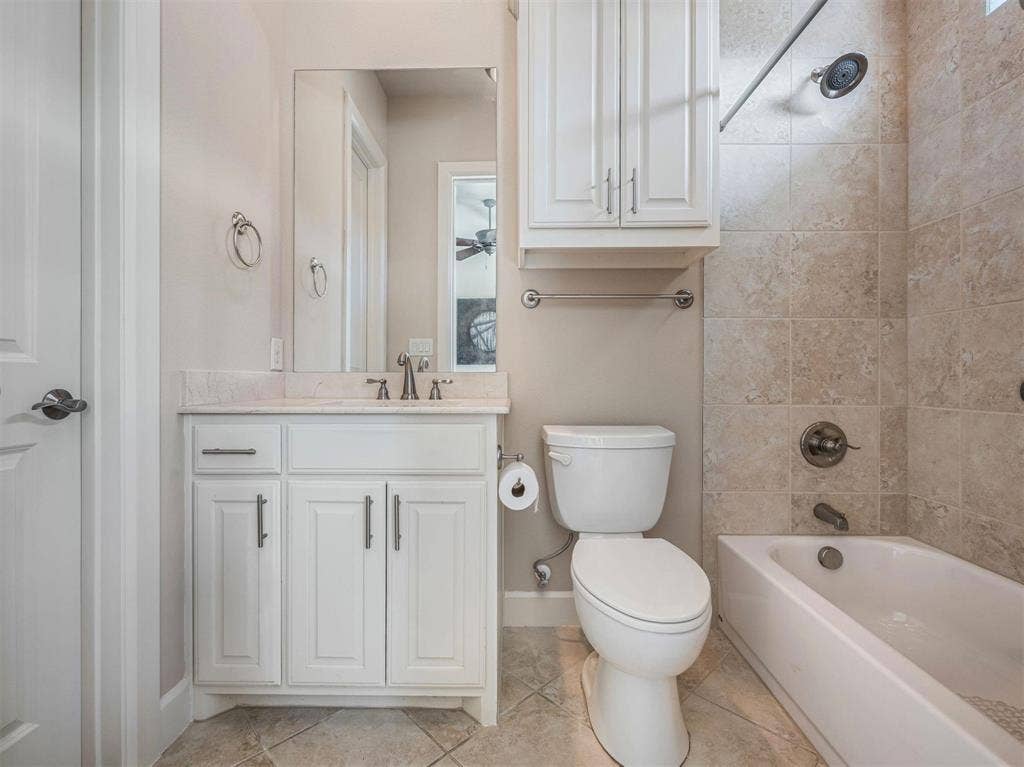 5001 Meridian Lane, #2103, Addison, TX 75001 Bathroom featuring a white vanity with a light-colored countertop, ceramic tile flooring, a built-in bathtub with tiled surround, and an overhead storage cabinet