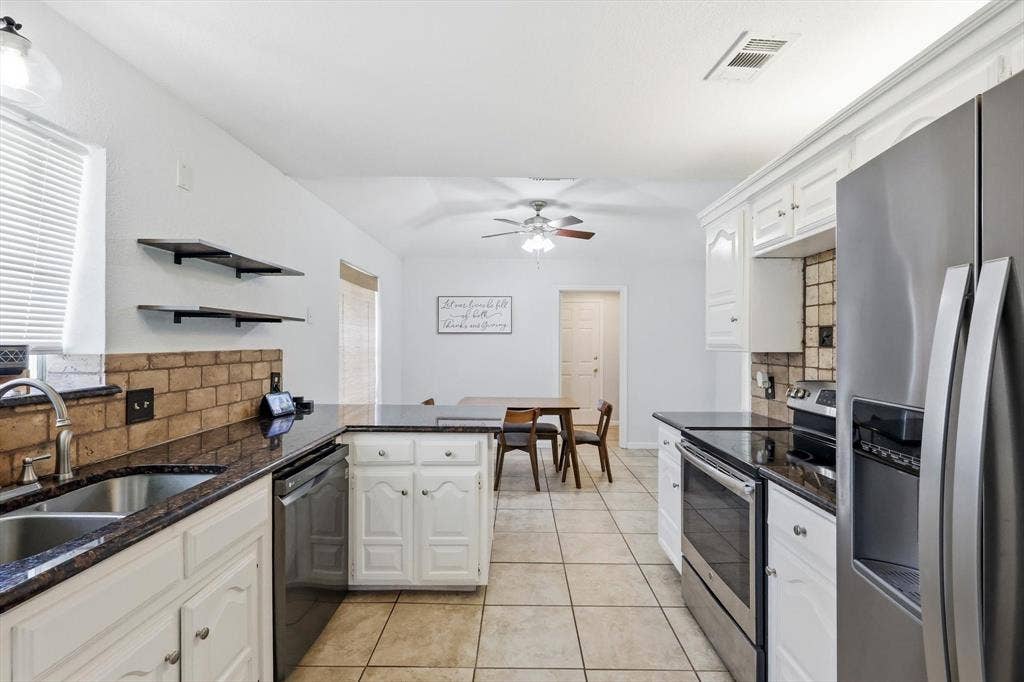 437 Bradshaw Street, Cedar Hill, TX 75104 Bright kitchen featuring white cabinetry, dark polished countertops, stainless steel appliances, brick-style backsplash, and tile flooring