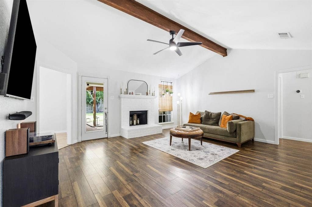 437 Bradshaw Street, Cedar Hill, TX 75104 Spacious living area featuring vaulted ceilings, exposed wood beams, a white brick fireplace, wood-finish flooring, and a ceiling fan