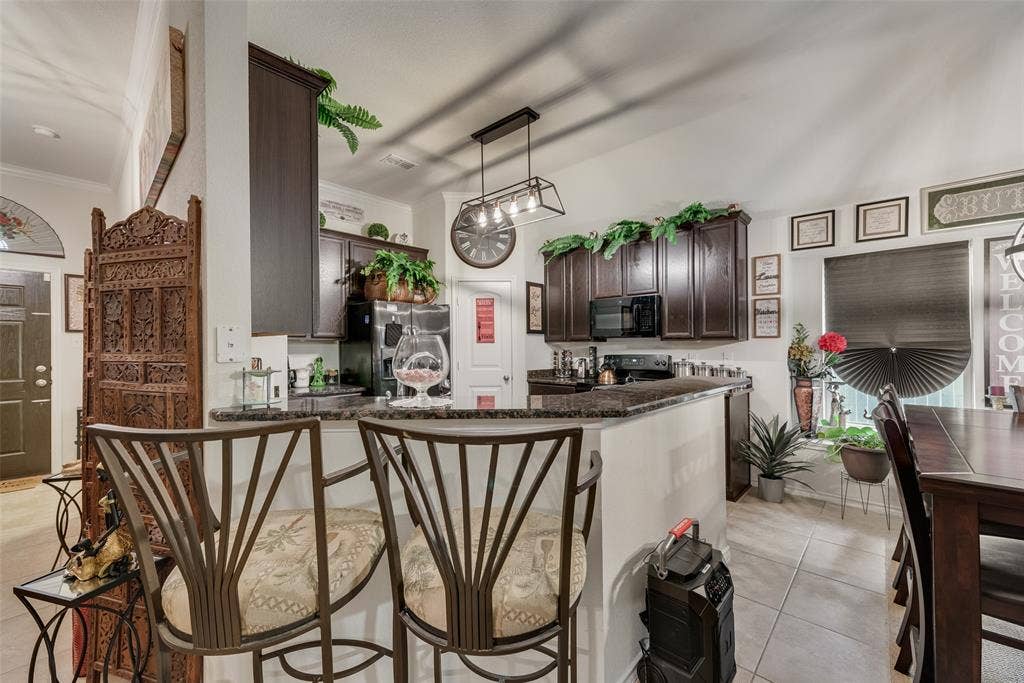 301 Billy Wickliffe Drive, Wilmer, TX 75172 Kitchen featuring a breakfast bar with stone-finish countertops, dark wood cabinetry, and a black appliance package
